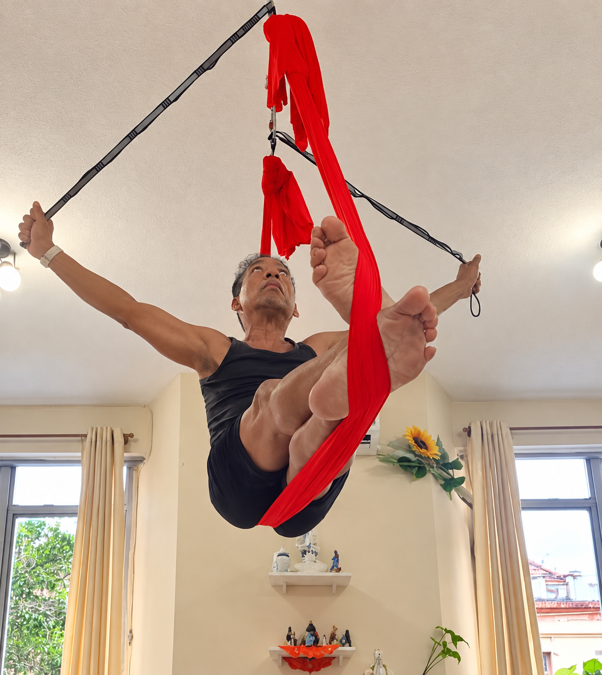Jair Fortes Rodrigues suspenso no tecido vermelho durante a prática de yoga aéreo.
